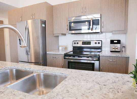 A kitchen with a stainless steel refrigerator, microwave, oven, and sink.