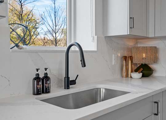 A modern kitchen with a stainless steel sink and white cabinets.