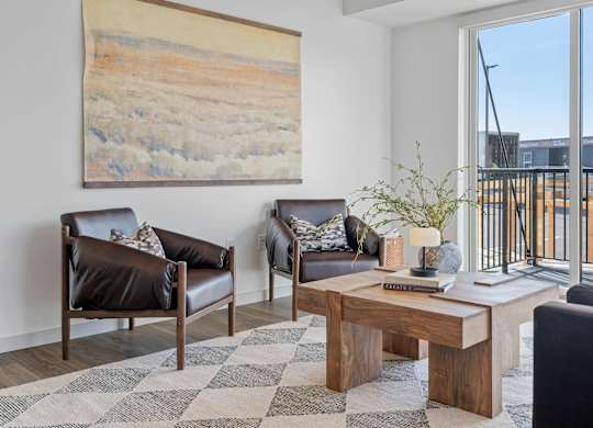 A living room with a brown leather couch, a wooden coffee table, and a large painting on the wall.