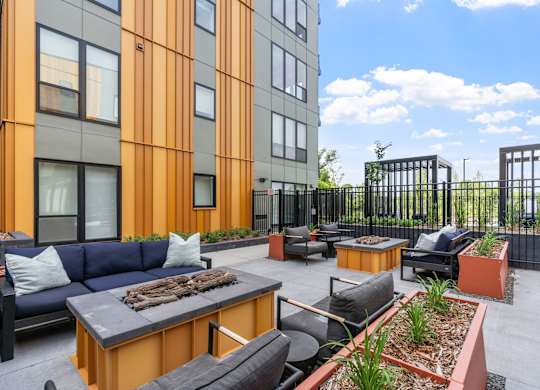 A patio area with a black table and chairs, a couch, and a fire pit.