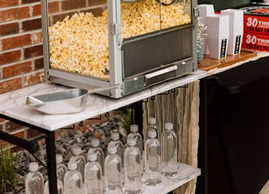 A red popcorn machine is on a table with bottles of water.