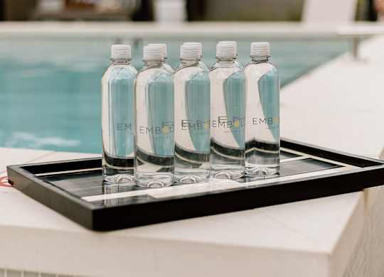 Four bottles of water are lined up on a tray by a pool.