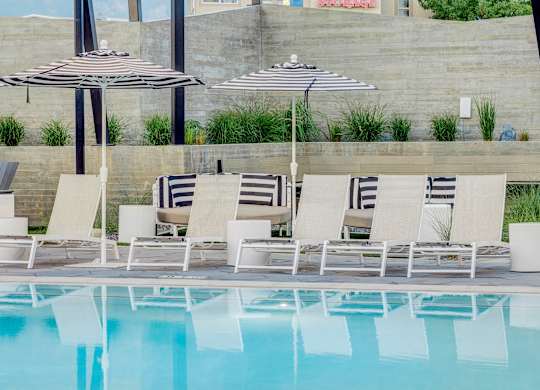A pool with chairs and umbrellas is surrounded by a wall.