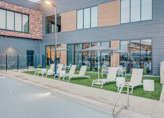 A modern building with a pool and lounge chairs.
