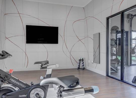A room with a treadmill and a television on the wall.