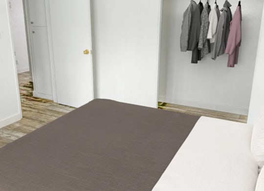 A room with a grey rug and clothes hanging on the wall.