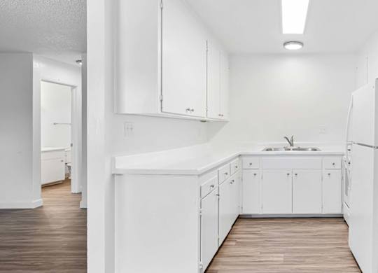 A white kitchen with a sink and a refrigerator.