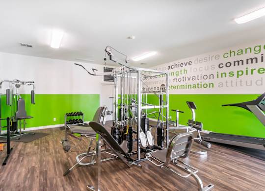 A gym with a green wall and a row of exercise machines at Chaparral Apartments, Palmdale