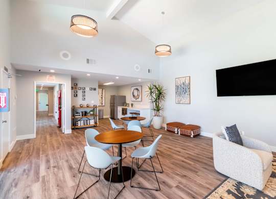 A living room with a TV on the wall and a dining table with chairs at Chaparral Apartments, Palmdale