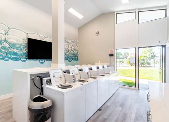 A row of washing machines are lined up in a room. at Chaparral Apartments, California, 93551