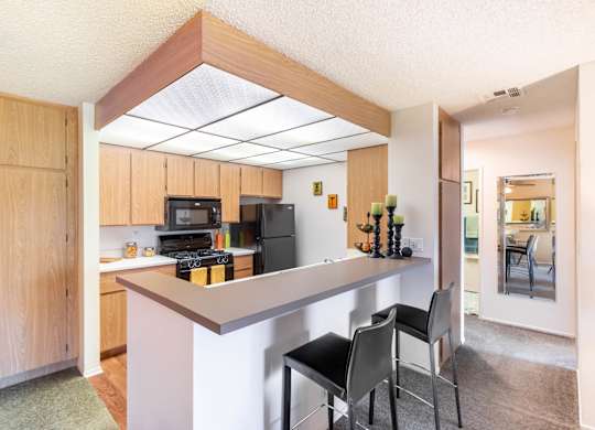 A kitchen with a white counter and black chairs. at Chaparral Apartments, Palmdale, CA, 93551