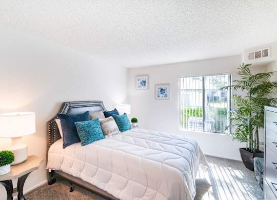 A bedroom with a large bed and a window with blinds at Chaparral Apartments, California, 93551
