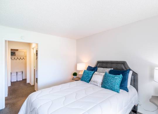A bedroom with a white bed and blue pillows. at Chaparral Apartments, Palmdale, California