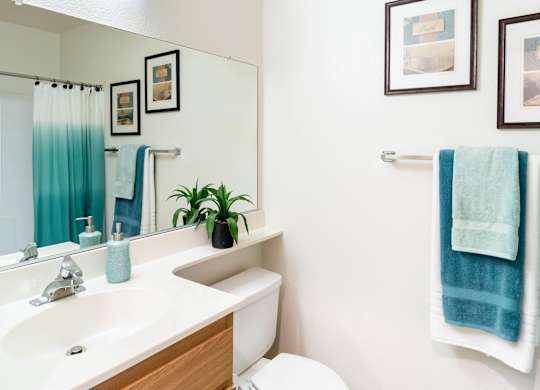 A bathroom with a toilet, sink, mirror, and pictures on the wall at Chaparral Apartments, Palmdale, California