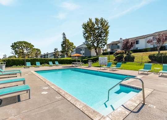 A swimming pool surrounded by lounge chairs and trees. at Chaparral Apartments, Palmdale, California