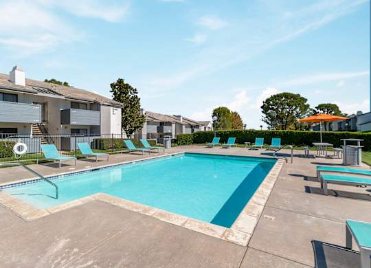 A swimming pool surrounded by lounge chairs and apartment buildings at Chaparral Apartments, Palmdale, CA