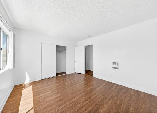 A room with white walls and wooden flooring with a window on the left.