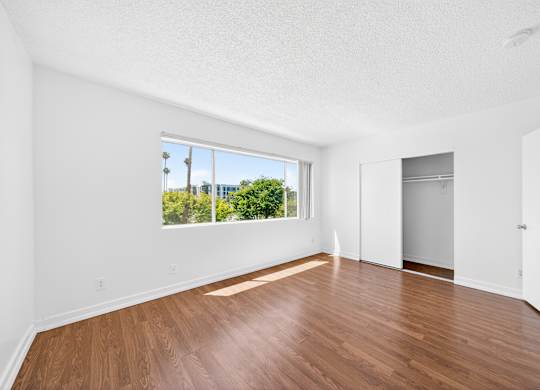 Empty room with wooden floors and a window overlooking a cityscape.