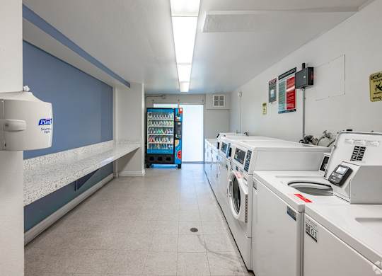 A laundromat with a row of washers and dryers at Oak Park Apartments, Monrovia, 91016
