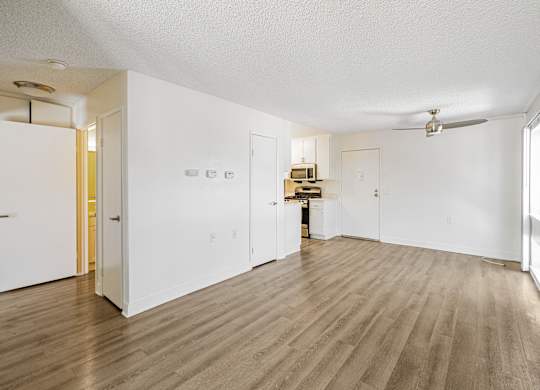 A room with white walls and wooden flooring with a ceiling fan.