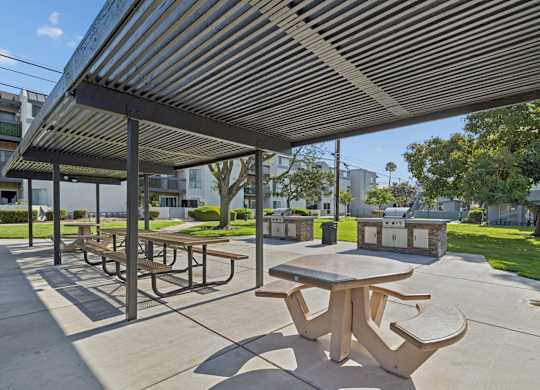 A patio with tables and benches under a striped awning.
