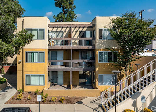 A yellow and beige apartment building with a staircase leading to the second floor at Oak Park Apartments, Monrovia, 91016