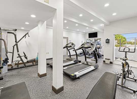 A well-lit gym with a variety of equipment including treadmills, stationary bikes, and weight machines.