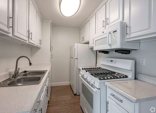 A white kitchen with a sink, stove, and refrigerator at Oak Park Apartments, Monrovia, 91016