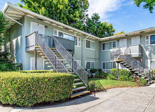 A sunny day at a two-story apartment building with a green lawn and trees.