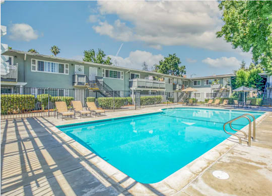 A swimming pool surrounded by a concrete deck and lounge chairs.