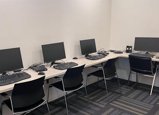 A room with a white desk and black chairs with a computer on it.