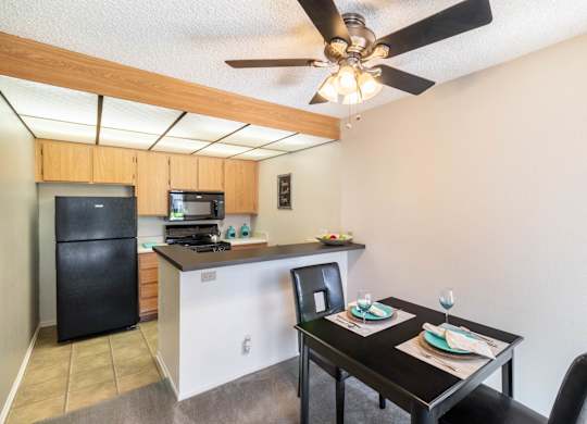 A kitchen with a black fridge and a black dining table with two chairs at Chaparral Apartments, California, 93551