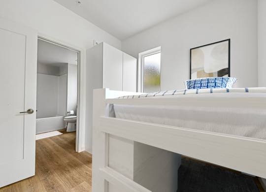A white bedroom with a bed and a mirror on the wall.