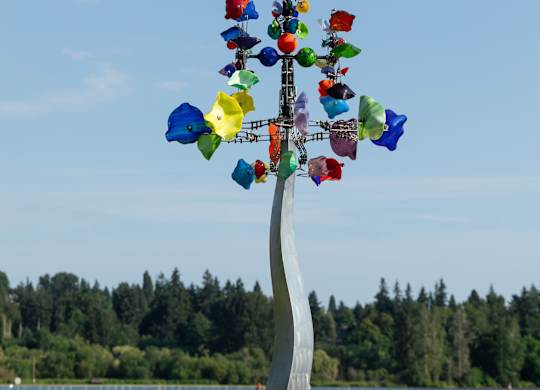 A person in a yellow dress is walking on a beach next to a tree with many flags on it.