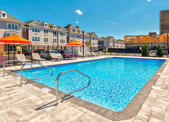 a swimming pool with chairs and umbrellas in front of apartment buildings at Solo at North Bergen, New Jersey