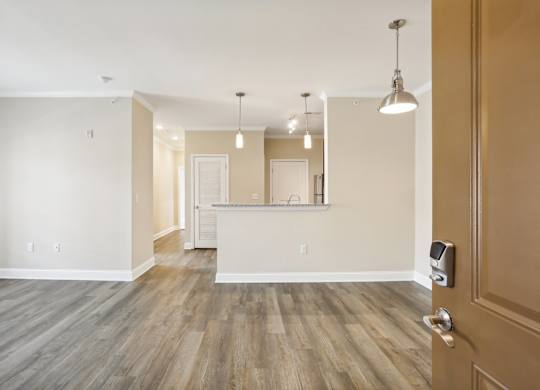 an empty living room with a kitchen in the background and a door open