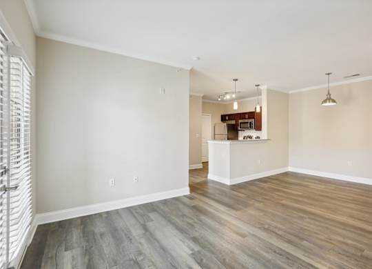an empty living room with wood flooring and a kitchen