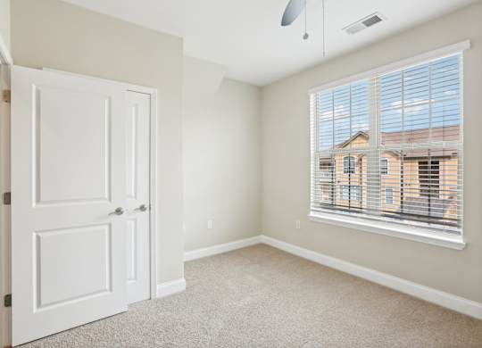 an empty bedroom with a large window and a white door