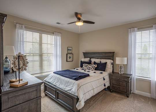 a bedroom with a bed and two windows and a ceiling fan