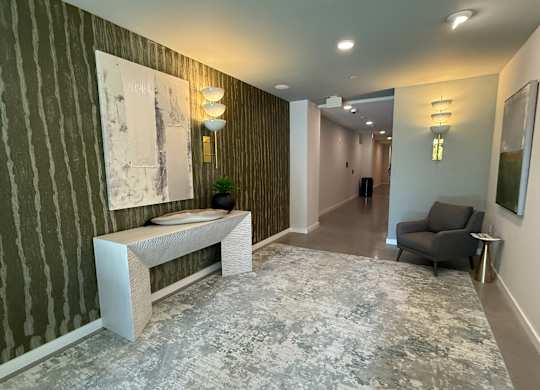 A hallway with a bench, a chair, and two paintings on the wall.