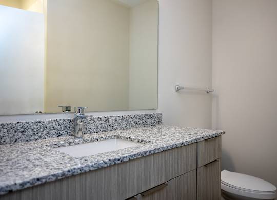 Modern bathroom at NOVI at Concord featuring a large mirror and sleek vanity with under-sink storage, and a combination bathtub and shower with white tile surround.