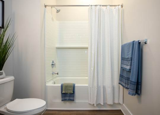 Modern bathroom at NOVI at Concord with bathtub and shower with white tile surround.