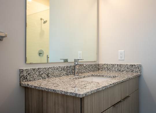 Modern bathroom at NOVI at Concord featuring a large mirror and sleek vanity with under-sink storage, and a combination bathtub and shower with white tile surround.