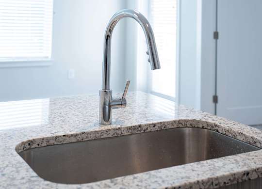 A modern kitchen sink with a chrome faucet and granite countertops at Novi Rise.