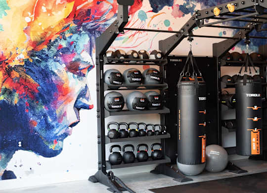 A gym with a punching bag, kettlebells, and a wall mural.