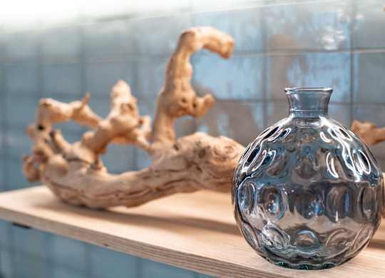 A blue glass vase sits on a shelf next to a piece of driftwood.