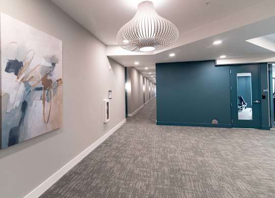 A hallway with a large painting on the wall and a carpeted floor.