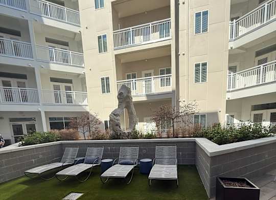 A sculpture sits in the middle of a grassy area in front of apartment buildings.