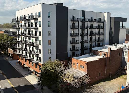 A modern apartment building with balconies is situated on a street corner.