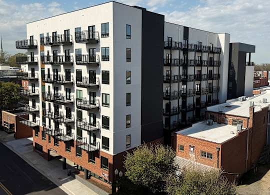 A modern apartment building with balconies is surrounded by other buildings.